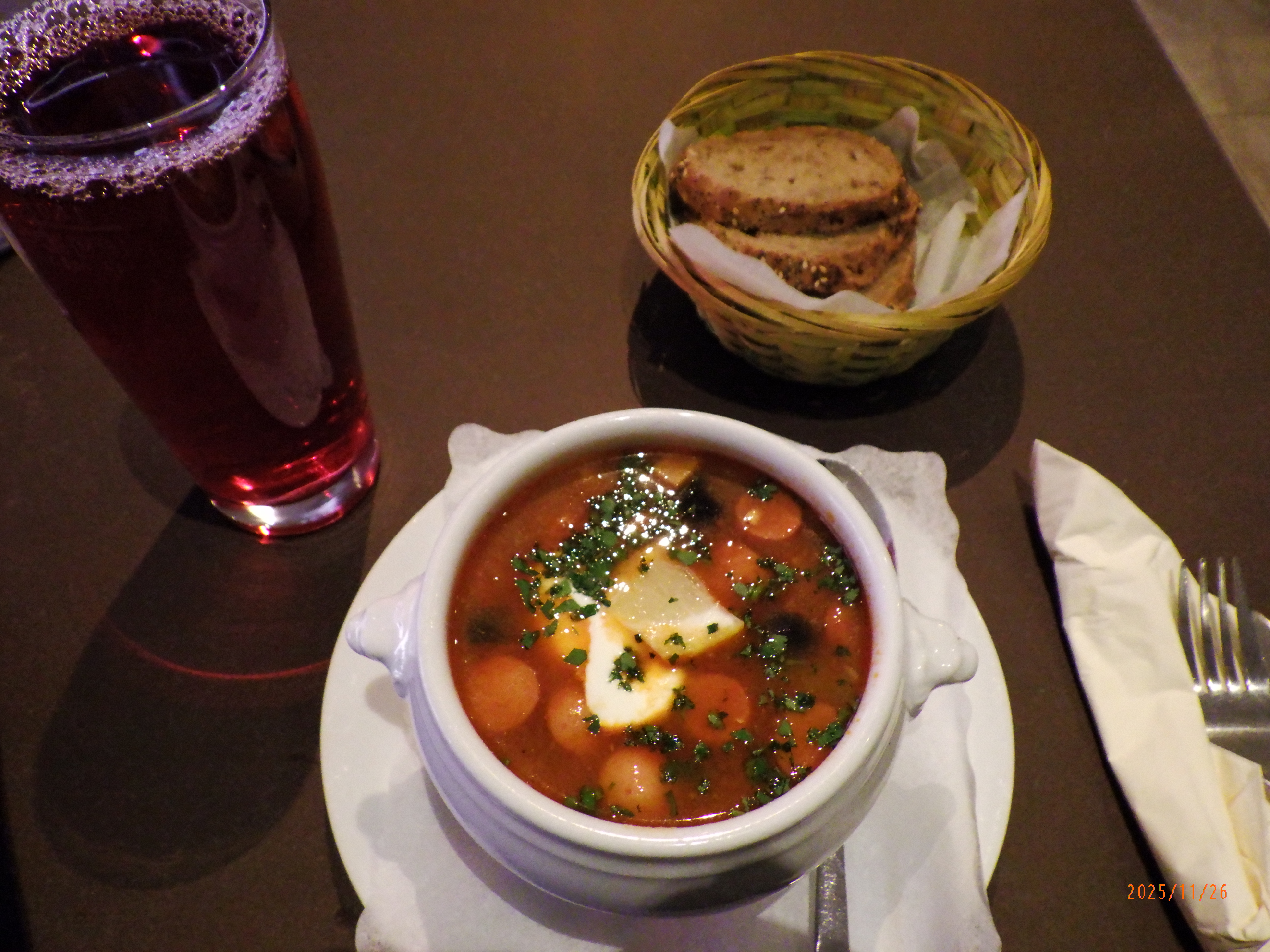 A bowl of solyanka soup with a glass of mors and a basket of bread