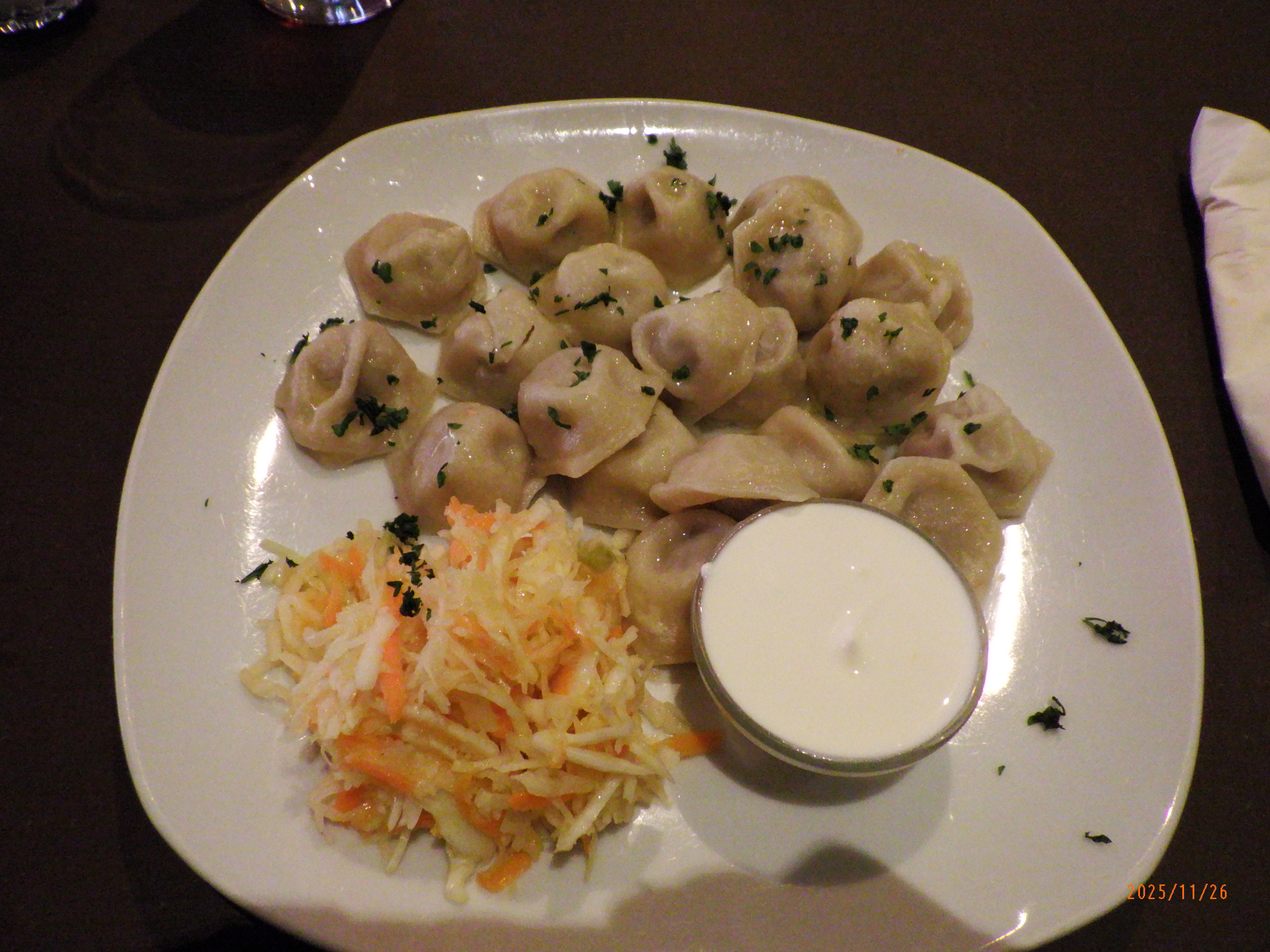 A plate of pelmeni with shredded salad and a small cup of sour cream